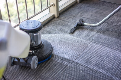 A vacuum and carpet floor buffer being used to clean a low pile commercial carpet